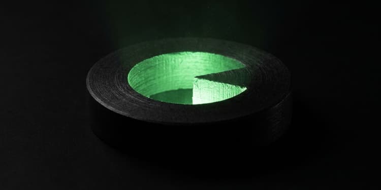 A black circular form with one wedge cut away, green light spilling out of the missing segment