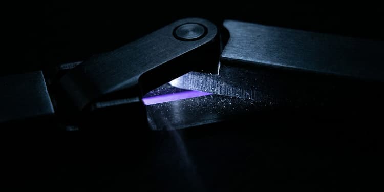 A close-up macro shot of a black mechanical toggle latch frozen mid-throw between two positions, with a narrow glowing violet line visible in the small gap between its contact points, set against a near-black background.