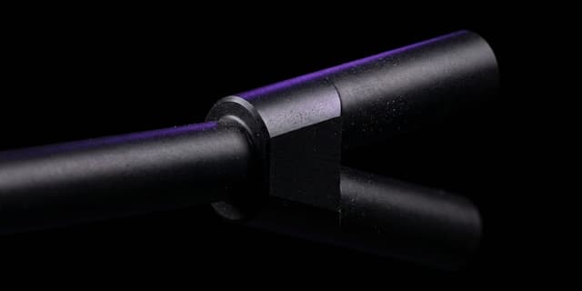 A close-up macro shot of a matte black machined rod splitting into two identical branches at a precision junction; one branch is lit with a thin violet edge of light, the other fades into blurred darkness.