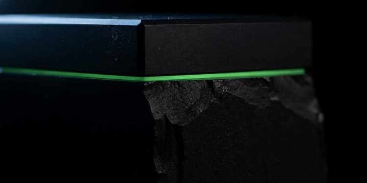 A matte black block split by a single thin green seam, a small finished section above it and a far larger rough mass falling away below