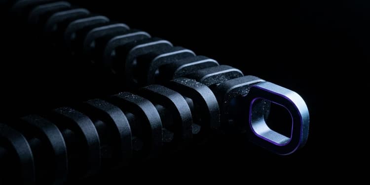 A chain of identical black machined links splits into two branches in near-total darkness; one branch fades into black while the other ends in a distinctly shaped link outlined by a thin violet glow.