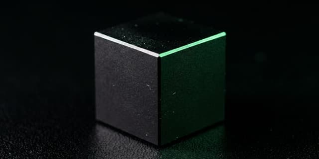 A sealed matte black cube with a single hairline seam glowing green, its contents not visible