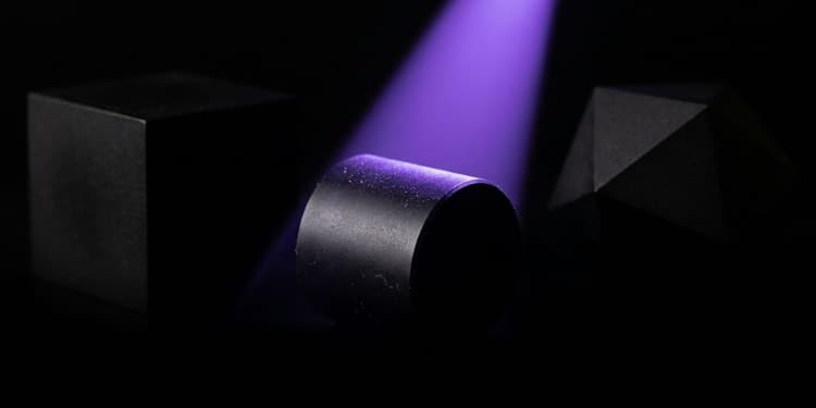 Three black forms of different geometry in a row, only the middle one lit by violet light