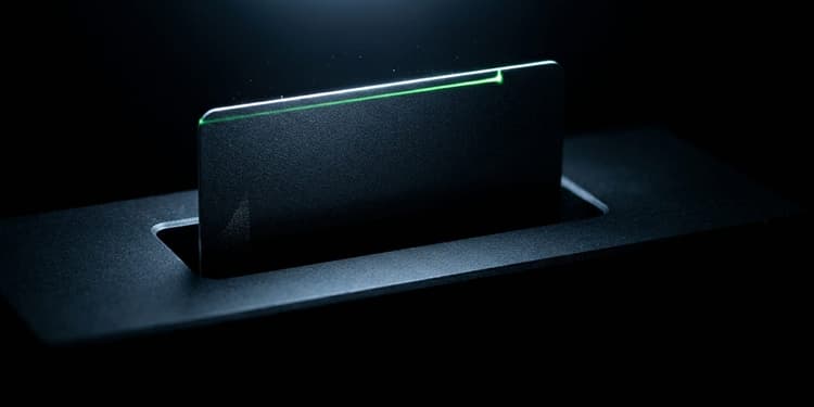 A matte black card is suspended halfway inside a dark machined slot, lit only along its top edge, with a thin green line running along the card that stops at the slot's opening, set against a near-black background.