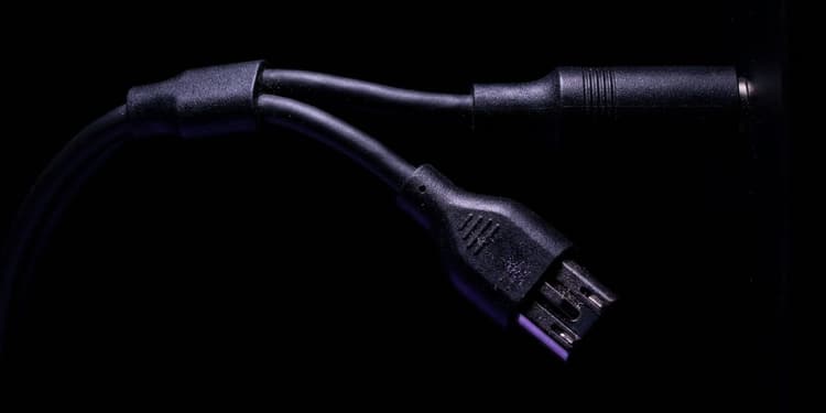 Macro shot of a black cable splitting into two branches; one branch is fully connected and fades into darkness, the other is pulled apart mid-disconnect with its exposed metal contacts lit in violet against an otherwise black background.