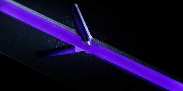 A single violet groove cut into black that divides into two diverging channels running to opposite edges