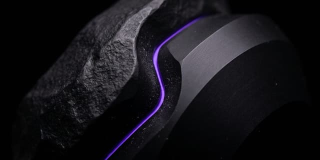 Two interlocking black forms, one rough-finished and one precision-ground, violet light along the seam between them