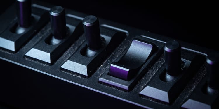 Close-up of a row of black toggle switches on a dark panel, lit with purple light, with visible dust specks.