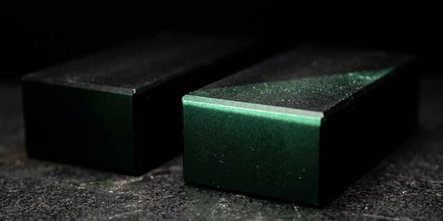 Two identical black blocks, one caught in a blade of green light and one just outside it, the gap between them closing
