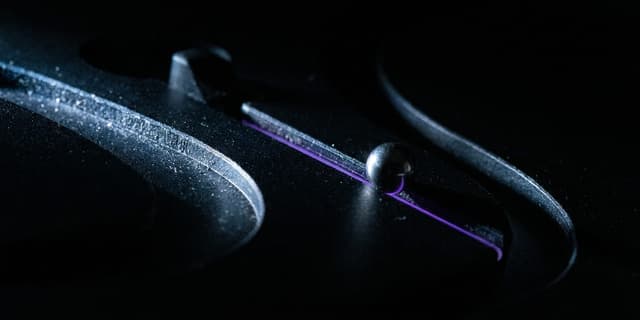 A macro shot of a dark mechanical track switch where a metal ball has rolled onto one branch, which glows faint violet, while the other branch sits empty and fades into darkness.