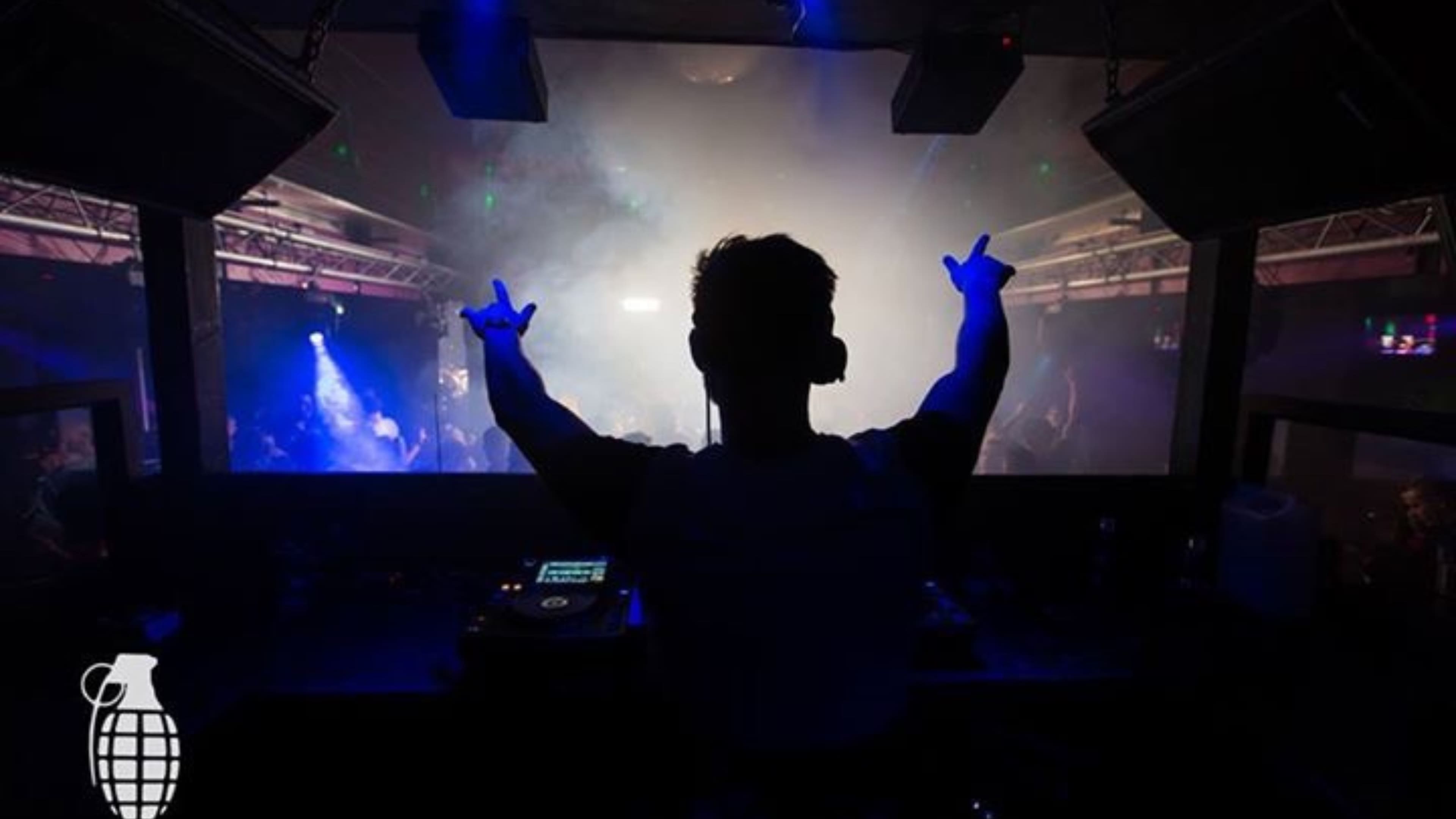 Silhouette of a DJ performing with arms raised under blue stage lights, 2014